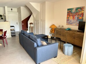 Ein Wohnzimmer mit einer Couch, einem Fernseher, einer Kommode und einem Bild an der Wand.