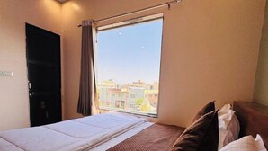 Una habitación de hotel con cama, ventana con vistas a edificios y puerta.