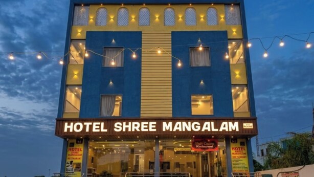 Un hotel con un cartel que dice 'HOTEL SHREE MANGALAM', un coche aparcado delante y asientos al aire libre.