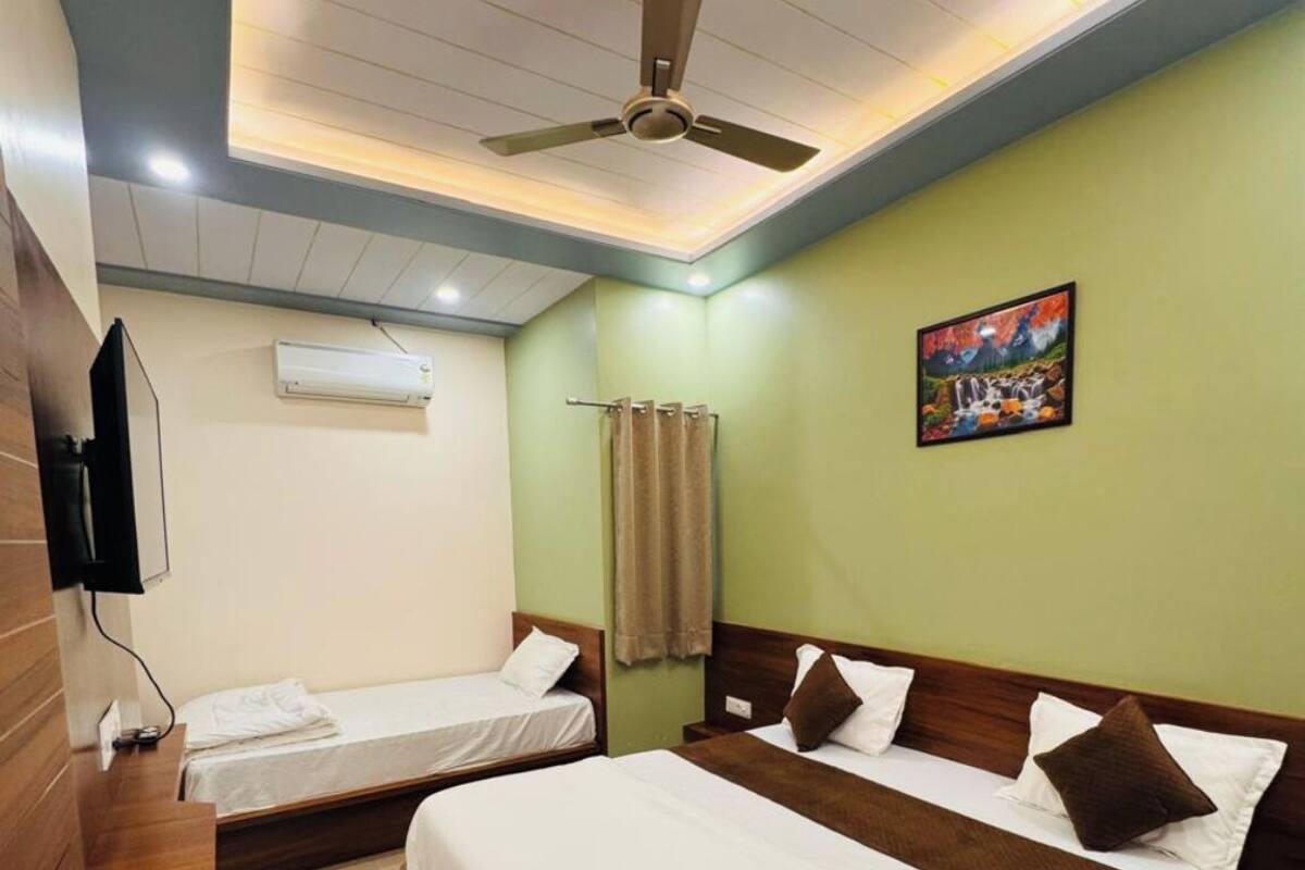A hotel room with two beds, a ceiling fan, an air conditioning unit, a painting on the wall, and a wooden side table.