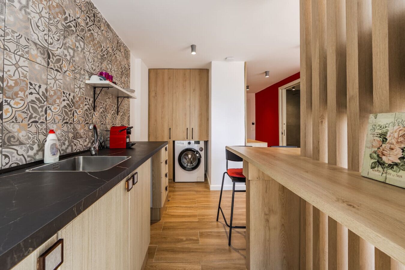 Eine kleine Küche mit Waschmaschine, einer Holztresen und einer roten Wand.