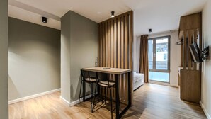 Ein modernes Zimmer mit Holzboden, einem kleinen Tisch mit zwei Stühlen, einem Bett und einem Fenster sowie einer Schiebetür.