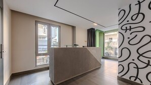 A modern reception area with a reception desk, large windows, and a green accent wall. - Orange Studio 104 | Love in Colours Collection by PikHost (Durrës)