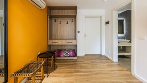 A hallway with a wooden bench, a small table, a wardrobe, and a bathroom visible through an open door. - Orange Studio 104 | Love in Colours Collection by PikHost (Durrës)