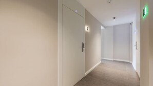 Un couloir doté de revêtements de sol en moquette, de murs blancs et de portes équipées d’interrupteurs.