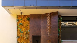 Entrada de um edifício moderno com piso de concreto, portão de metal e jardim vertical à esquerda.