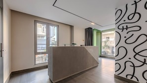 Uma área de recepção moderna com balcão, grandes janelas e uma parede verde de destaque.