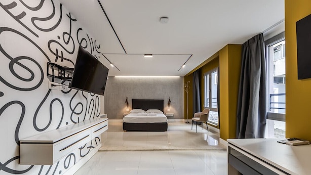Quarto de hotel moderno com uma cama grande, televisão de tela plana na parede, escrivaninha com cadeira e uma janela ampla com cortinas.