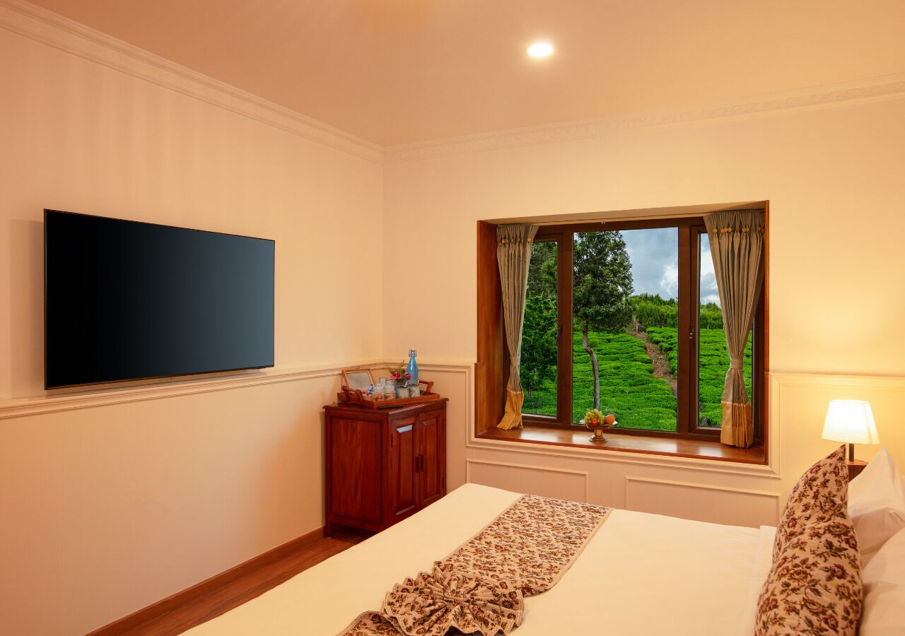 Une chambre d’hôtel avec un lit, un téléviseur fixé au mur, une fenêtre avec des rideaux et une petite table avec une lampe.