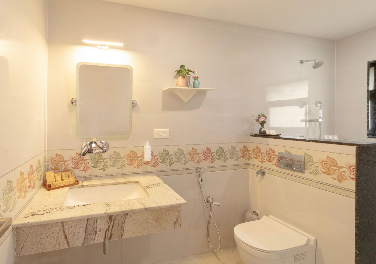 Un baño con lavamanos, espejo, ducha, inodoro y azulejos decorativos.