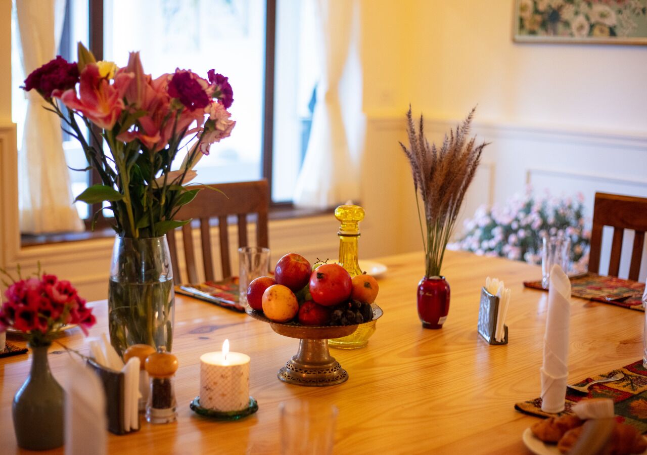 A dining table with a vase of flowers, a candle, a fruit bowl, and a candle holder.