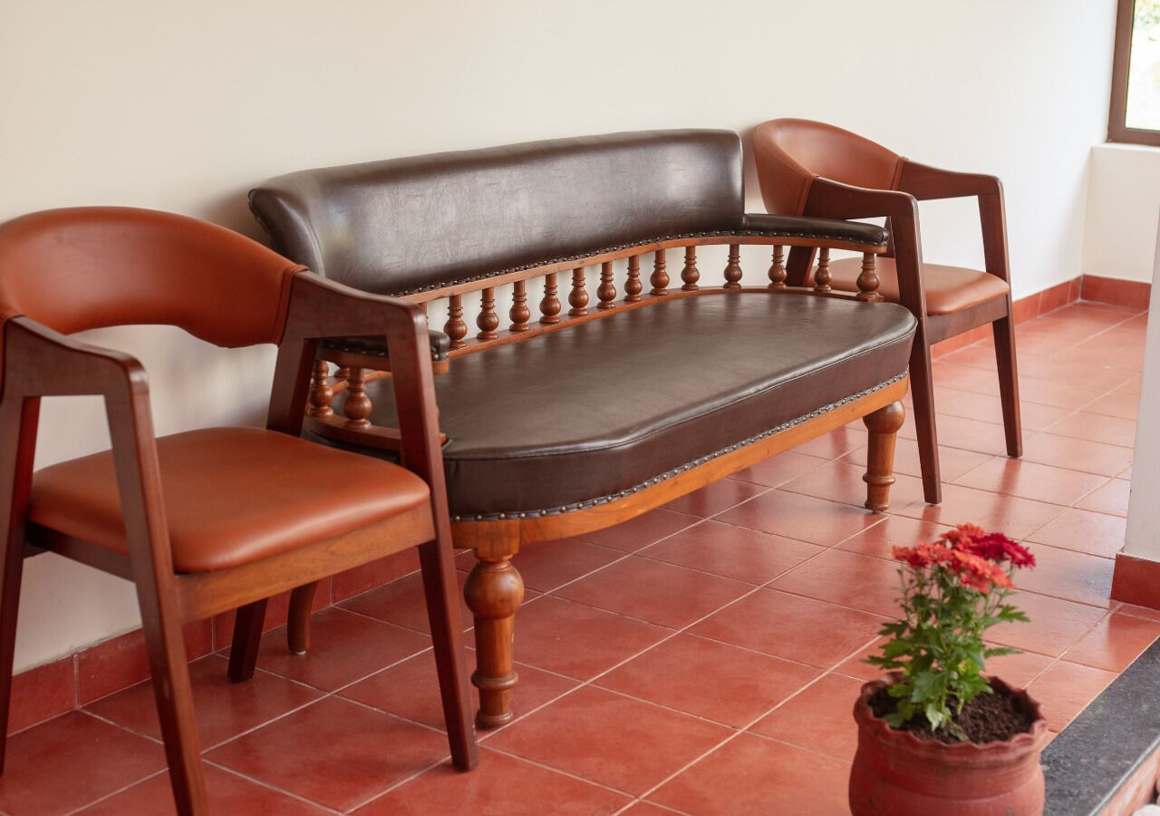 A wooden sofa with a cushioned seat and backrest, two wooden armchairs, and a potted plant with flowers.