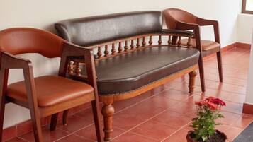 A wooden sofa with a cushioned seat and backrest, two wooden armchairs, and a potted plant with flowers.
