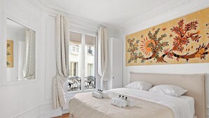 A hotel room with a bed, a large window with curtains, a painting on the wall, and a balcony with a wrought iron railing. - Luxurious apartment 3BDR/6P - Tour Eiffel (Paris)