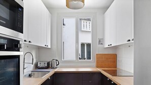 A compact kitchen with white cabinets, a built-in oven, a toaster, and a window with a view. - Luxurious apartment 3BDR/6P - Tour Eiffel (Paris)