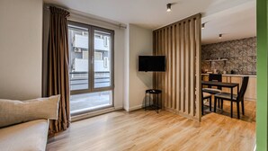 Ein modernes Wohnzimmer mit Sofa, Esstisch, Fernseher und einem durch eine Glastür einsehbarer Küchenbereich.