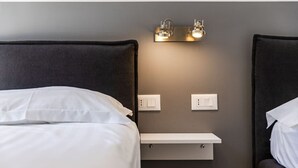 A hotel room with two beds, a bedside table, wall-mounted light fixtures, and a switchboard. - Brown Studio 116 | Love in Colours Collection by PikHost (Durrës)