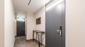 A hallway with a dark door labeled 116, a lighted exit sign, and a small table with a metal frame. - Brown Studio 116 | Love in Colours Collection by PikHost (Durrës)