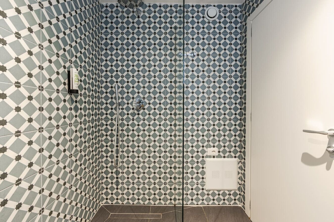 Ein Badezimmer mit Wandfliesen in geometrischem Muster, einer Duschkabine und einer weißen Tür.