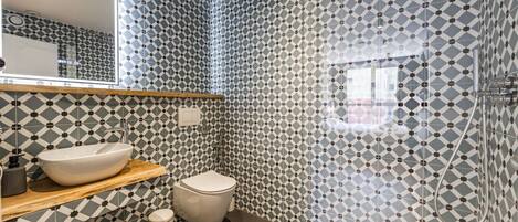 A bathroom with a geometric patterned tile wall, a white sink, a toilet, and a shower.