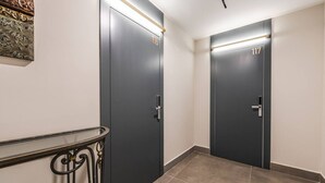 Ein Flur mit zwei dunkel gefärbten Türen, die mit 116 und 117 beschriftet sind, einem Metallgeländer und einem gefliesten Boden.