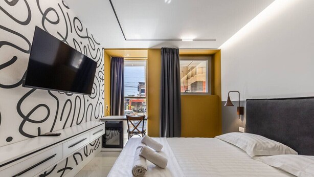 Ein Hotelzimmer mit Bett, Schreibtisch, Stuhl, Fernseher und einem Fenster mit Vorhängen.