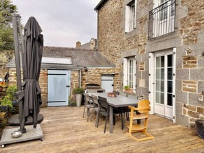 Een stenen huis met terras, tafel, stoelen en een barbecue.