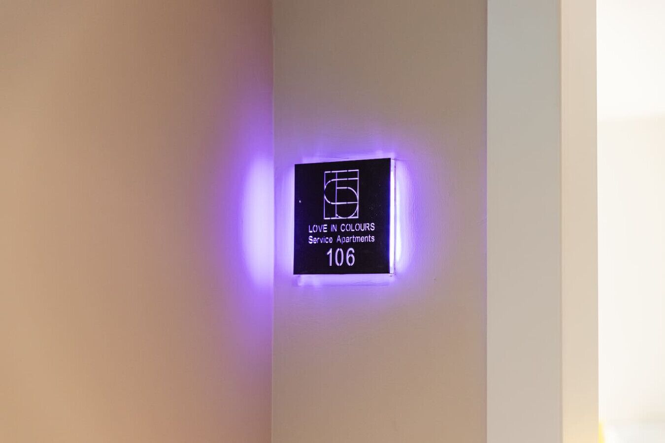 A wall-mounted sign with a purple glow, indicating 'Love in Colours Service Apartments 106.'