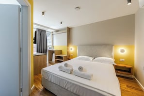 A hotel room with a large bed, bedside tables, a desk, and a wardrobe. - Yellow Studio 106 | Love in Colours Collection by PikHost (Durrës)