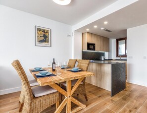A dining area with a wooden table and wicker chairs, a kitchen with wooden cabinets, and a framed picture on the wall. - Sole Mio - Sea View - Terrace - Pool (Fuengirola)