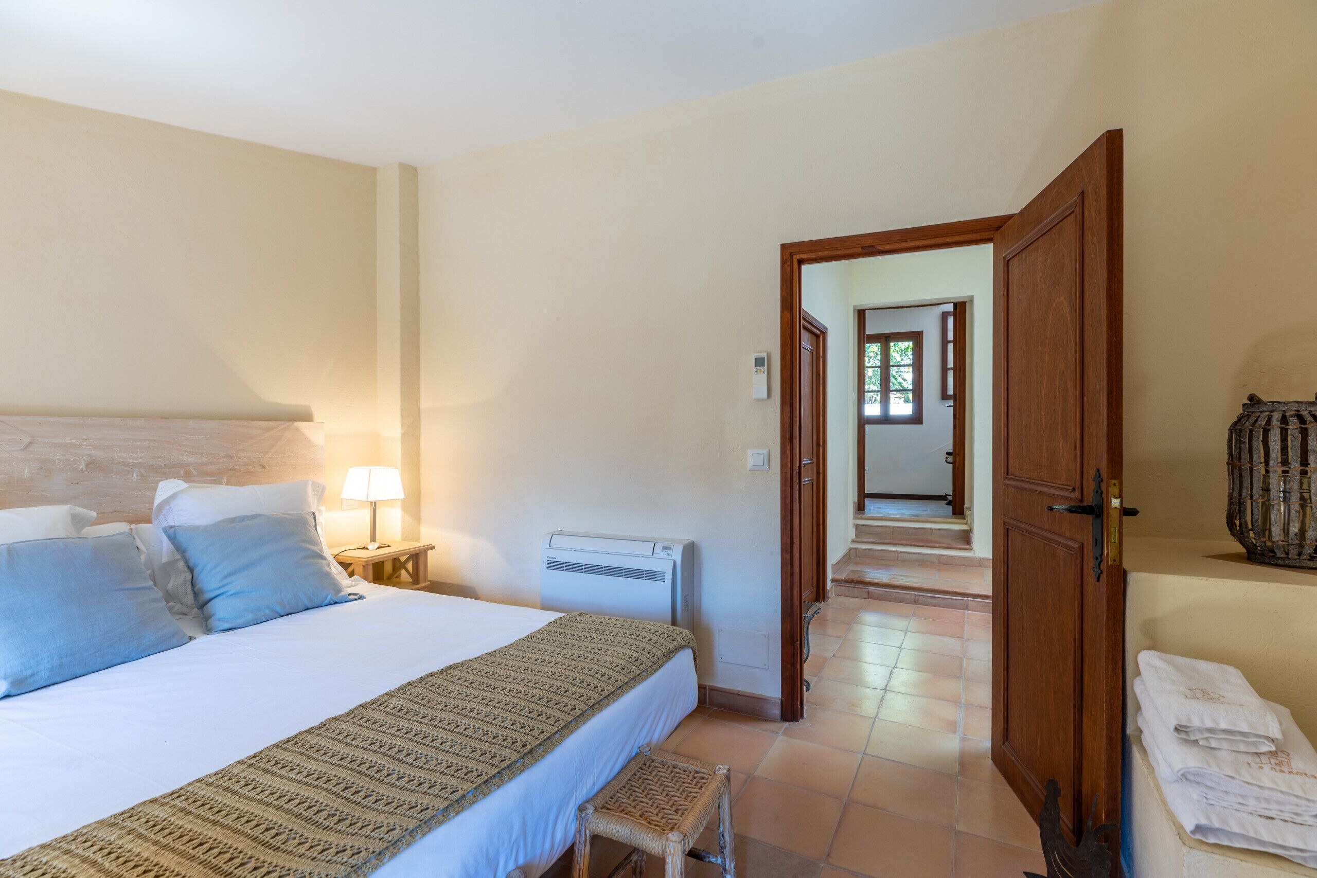 A bedroom with a bed, bedside lamp, air conditioning unit, and a view of a hallway.