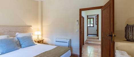 A bedroom with a bed, bedside lamp, air conditioning unit, and a view of a hallway.