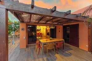 Een buiten eethoek met een houten pergola, een glazen tafel en rode stoelen.