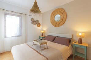 Ein Schlafzimmer mit einem Bett, Nachttischen, einer Hängeleuchte, einem runden Spiegel und einem Fenster mit Vorhängen.