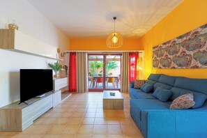 Ein Wohnzimmer mit Fernseher, Sofa, Couchtisch und Blick ins Freie.