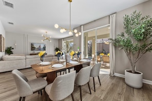 Un salon moderne avec un coin repas, une grande plante en pot et une vue à travers une porte vitrée.