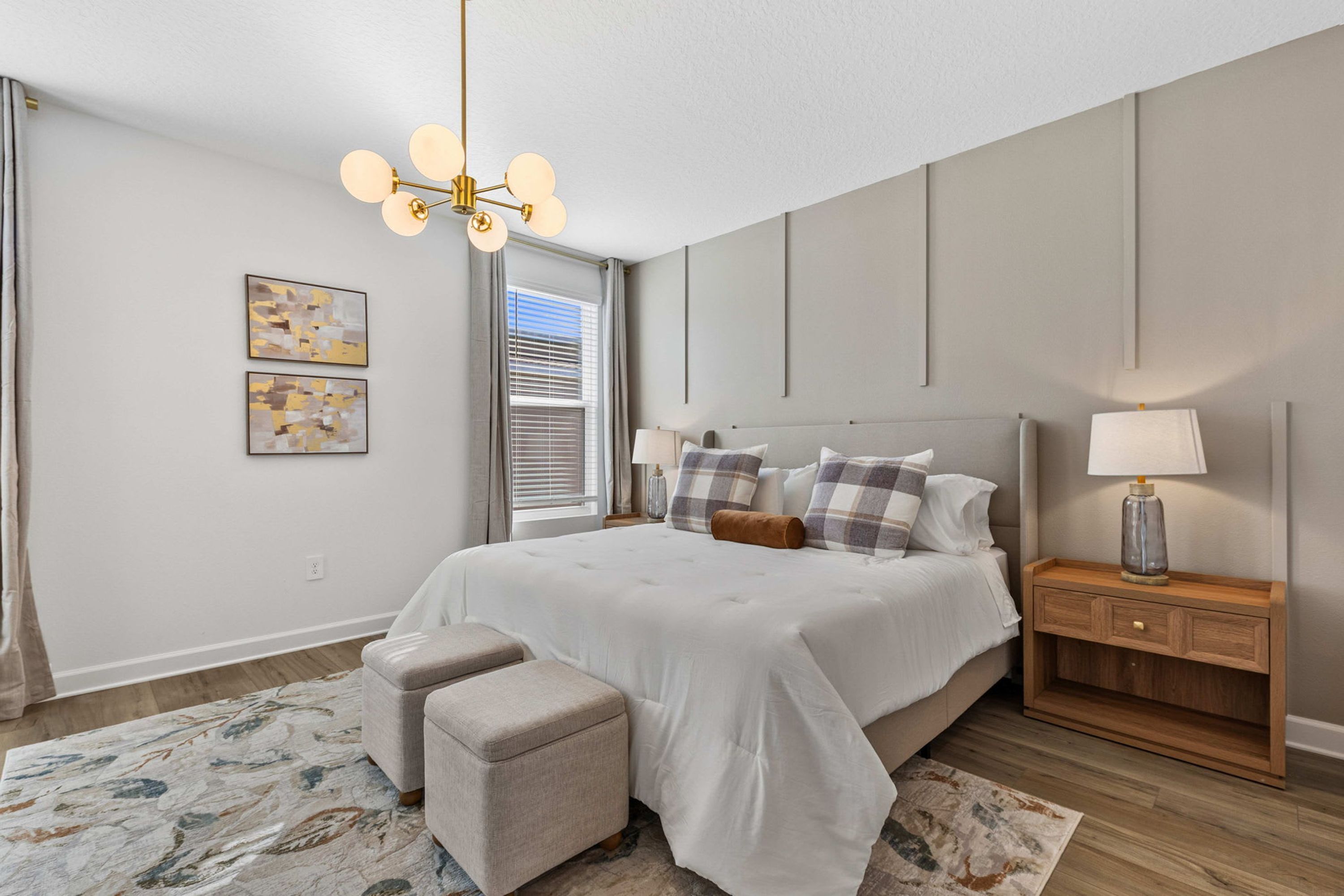 A bedroom with a large bed, a nightstand, a lamp, a chair, and artwork on the wall.
