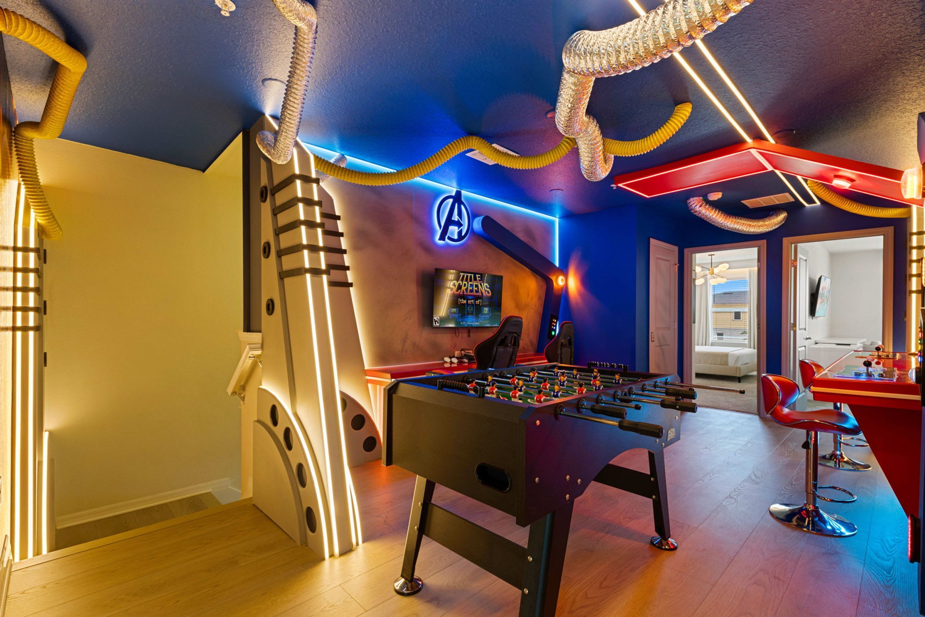 A room with a foosball table, a TV, and a wall-mounted screen displaying a movie.