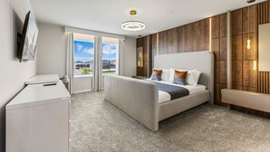 Ein modernes Hotelzimmer mit Bett, Schreibtisch, Fernseher und einem großen Fenster mit Blick auf die Stadt.