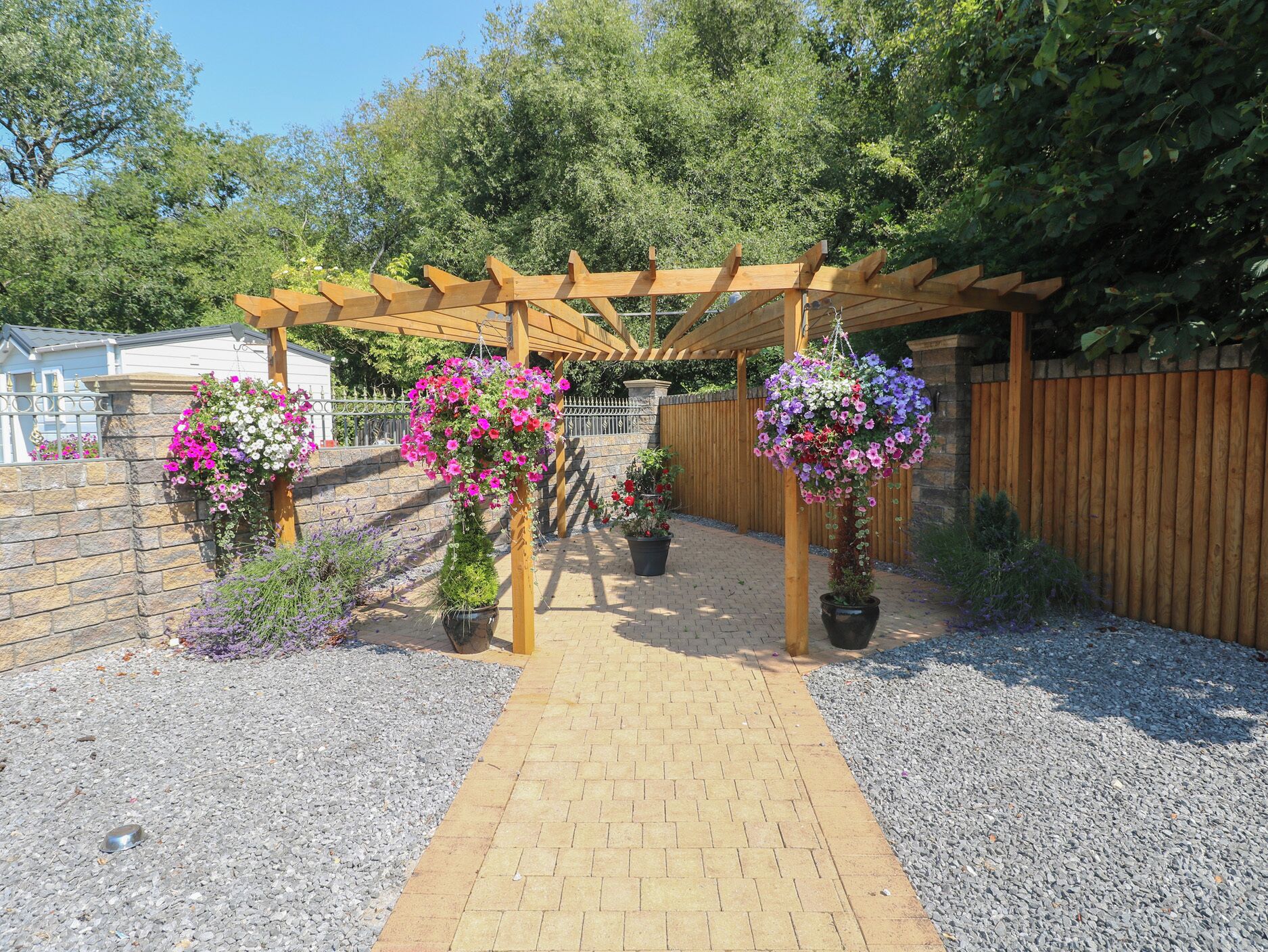 A garden pathway leading to a wooden pergola with hanging flower baskets.