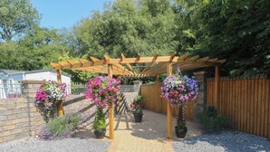 Un sentier de jardin menant à une pergola en bois ornée de suspensions de jardinières fleuries.