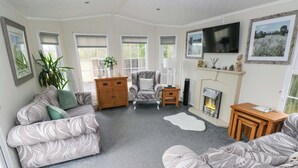 Un salon avec un canapé, un fauteuil, une cheminée, un téléviseur et une plante.