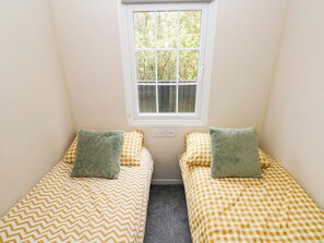 Una habitación pequeña con dos camas individuales, una ventana y un enchufe en la pared.