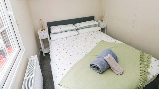 Une petite chambre à coucher, bien rangée, avec un lit, deux tables de chevet, une fenêtre et un radiateur.