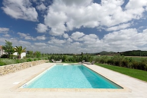 A rectangular swimming pool with clear blue water, surrounded by a stone wall and a grassy area with a stone pathway leading to it. - Podere La Sassicaia – Villa with Private Pool in the Tuscan Hills (Manciano)
