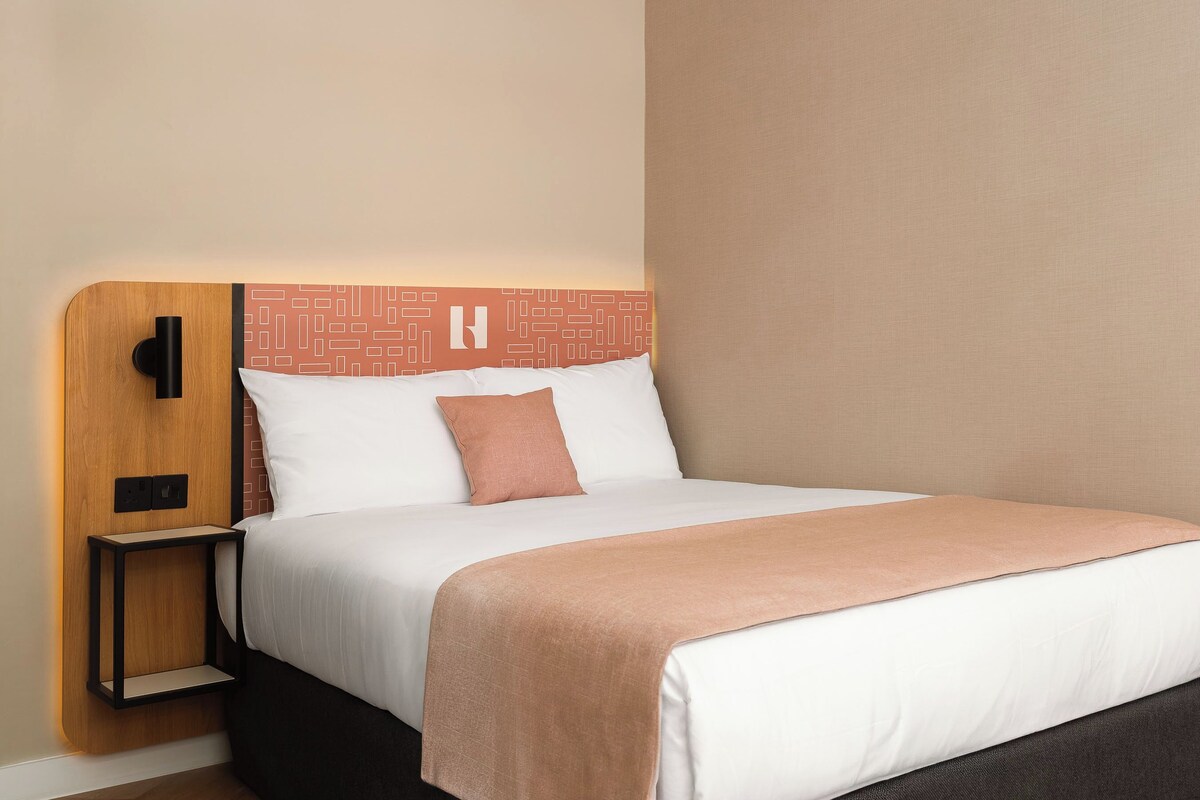 Een hotelkamer met een bed, nachtkastje en een lamp aan de muur.