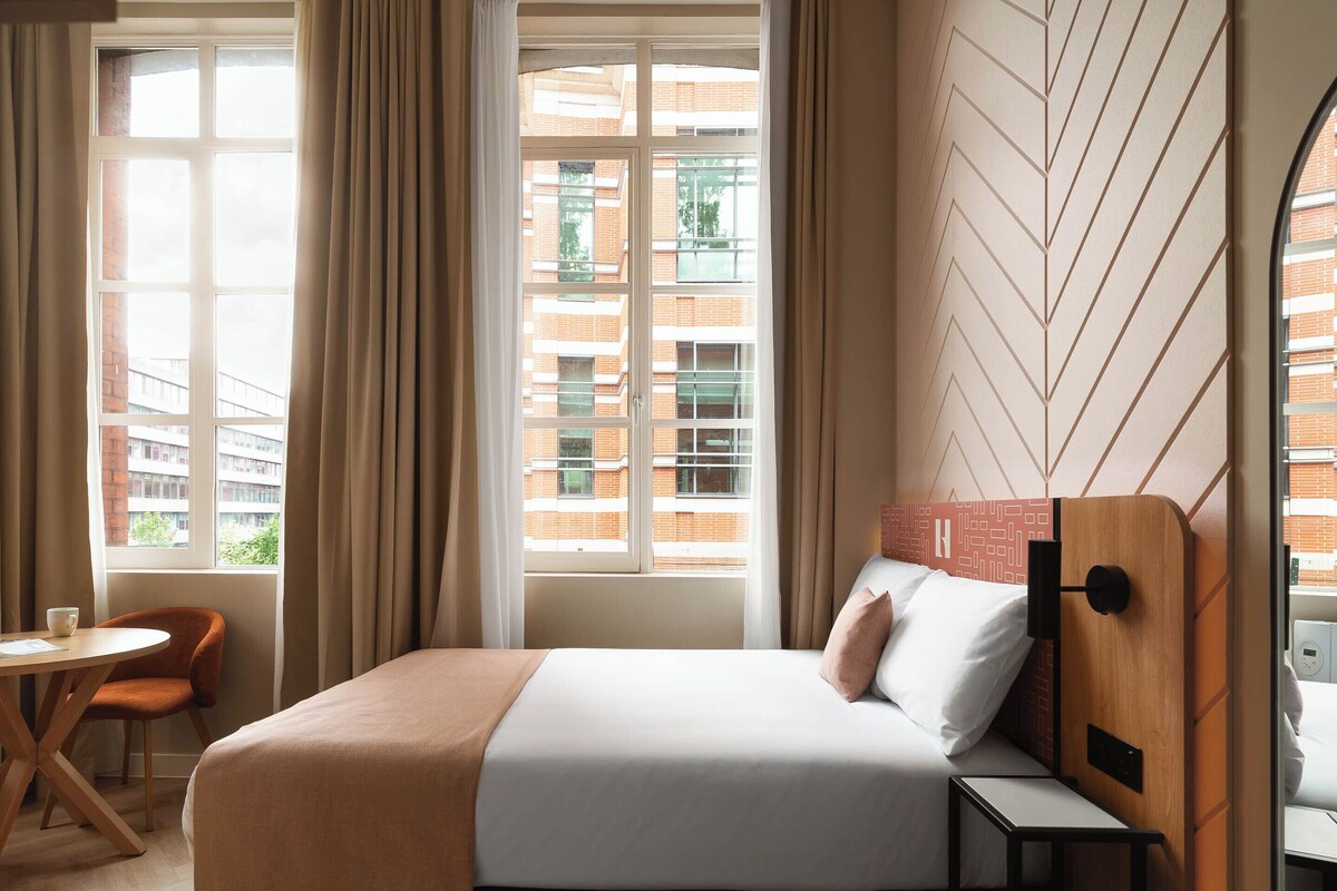 Een hotelkamer met een bed, een stoel, een tafel en een raam met gordijnen.