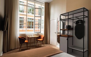 A hotel room with a bed, a desk with two chairs, a wardrobe, and a window with curtains. - Limehome London St. Paul's (London)
