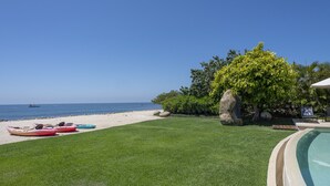 A pool area with a view of the beach, a well-maintained lawn, and a large rock. - Casa del Muelle in Punta Mita (Punta de Mita)