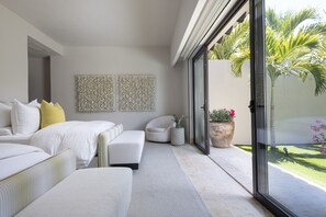 A modern bedroom with a bed, a sofa, a chair, and a large sliding glass door leading to a garden. - Casa del Muelle in Punta Mita (Punta de Mita)